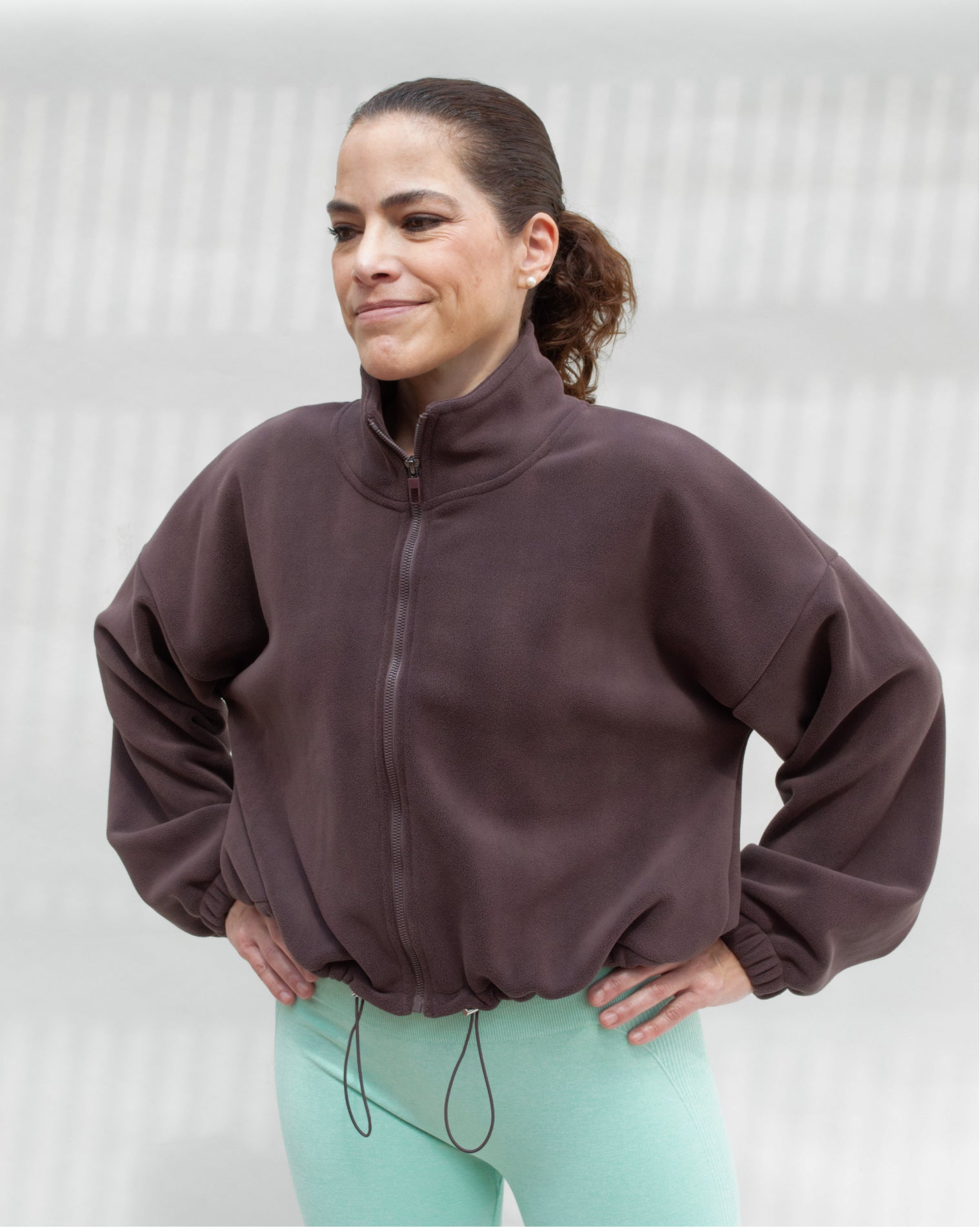 Chamarra deportiva oversize para mujer en tono café con cierre frontal y ajuste inferior regulable, confeccionada en tela afelpada de tacto suave, ideal para brindar abrigo ligero y comodidad antes o después del entrenamiento.