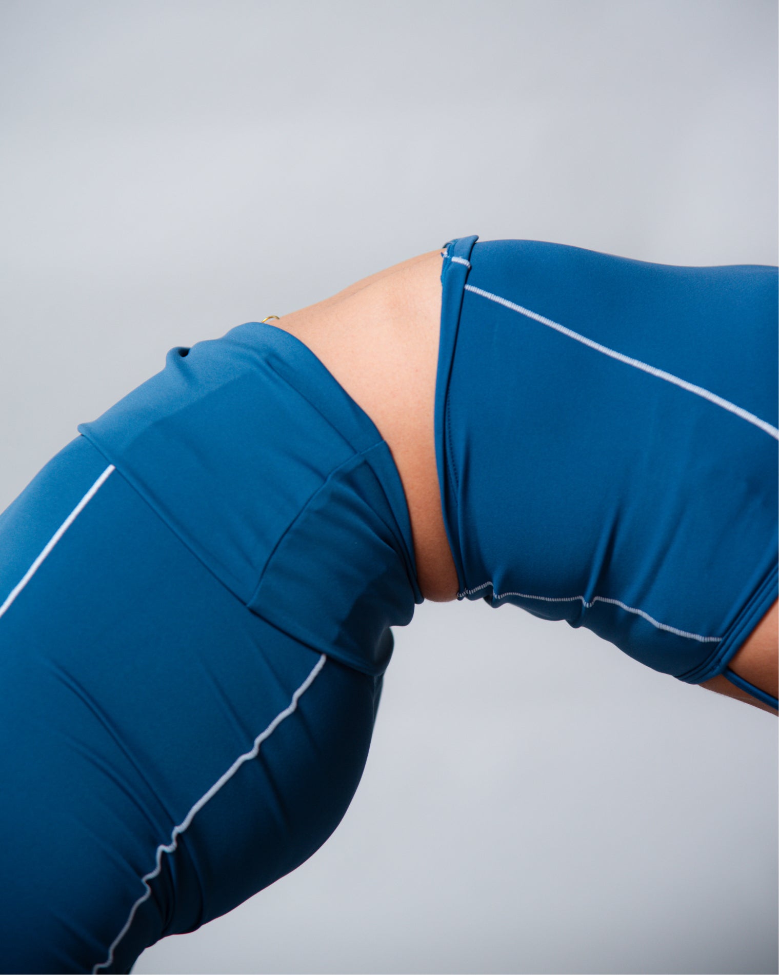 Leggings deportivos color azul de tiro alto con diseño liso y costuras visibles en contraste, ajuste ceñido al cuerpo y acabado uniforme, mostrados en vista posterior como parte de un conjunto deportivo.