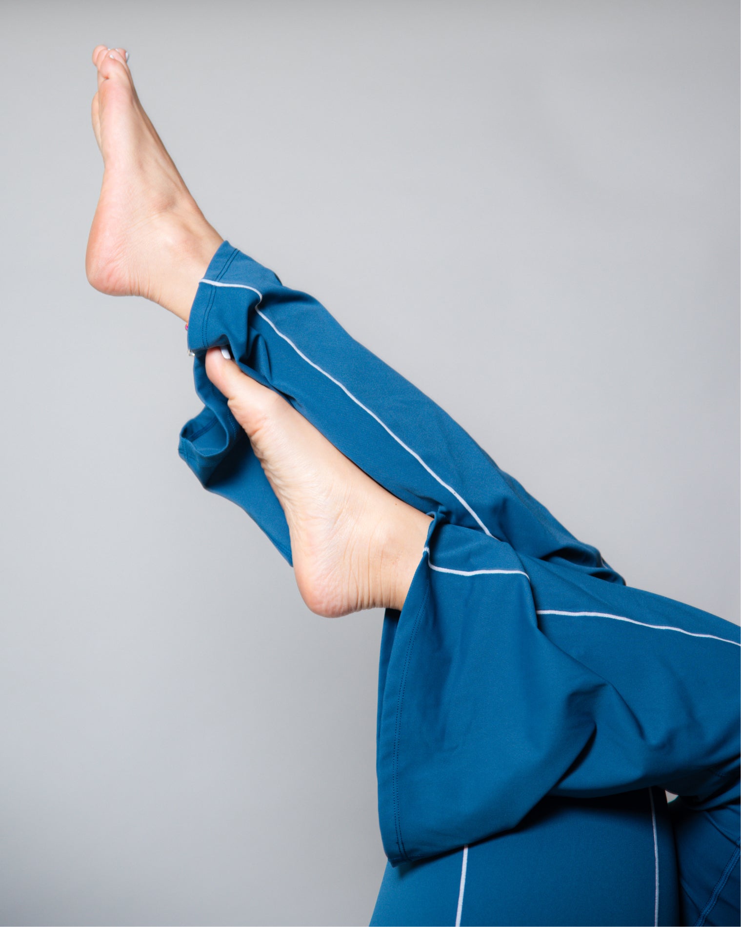 Leggings deportivos color azul de tiro alto con diseño liso y costuras visibles en contraste, ajuste ceñido al cuerpo y acabado uniforme, mostrados en vista posterior como parte de un conjunto deportivo.