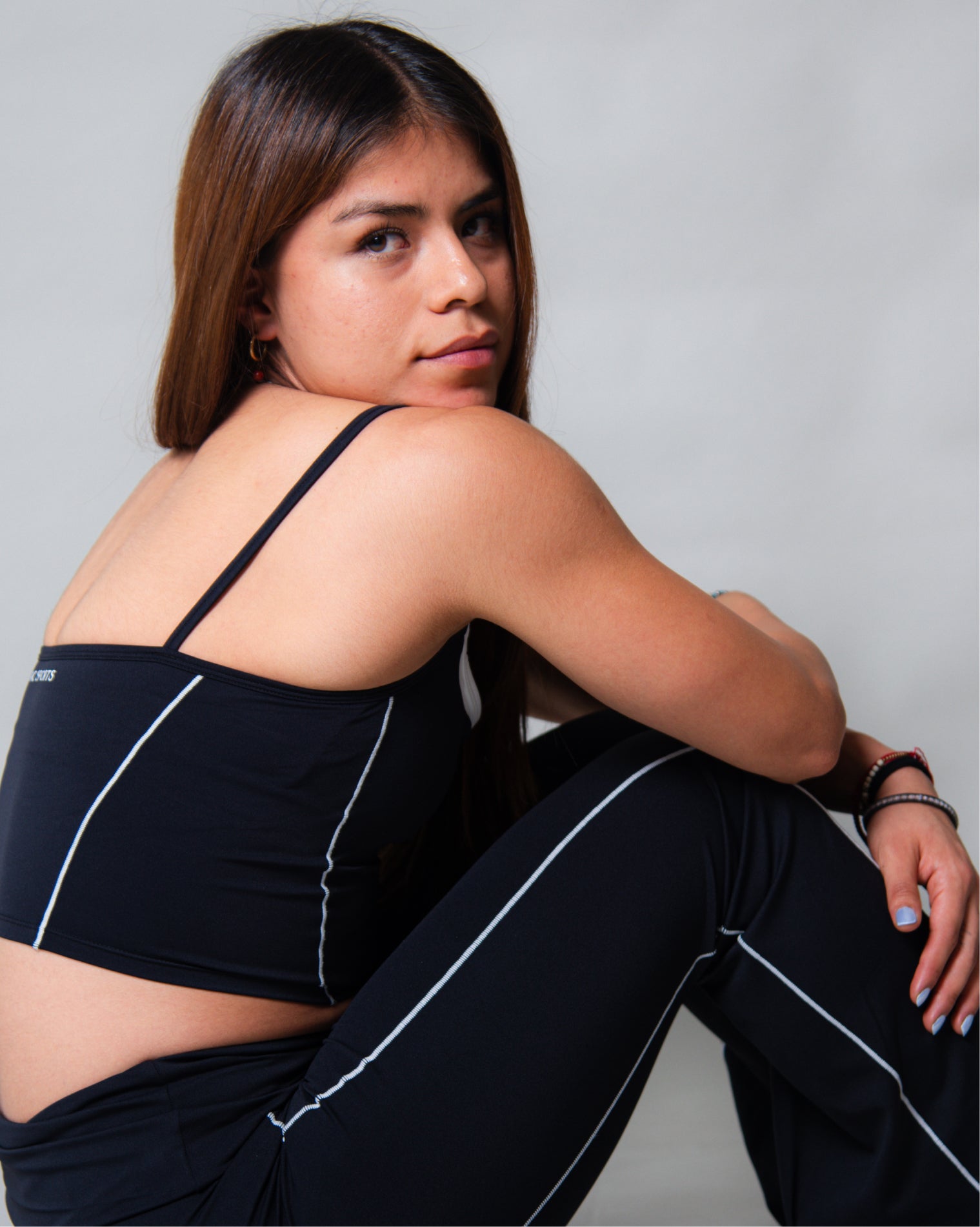 Leggings deportivos color negro de tiro alto con diseño liso y costuras visibles en contraste, ajuste ceñido al cuerpo y acabado uniforme, mostrados en vista posterior como parte de un conjunto deportivo.