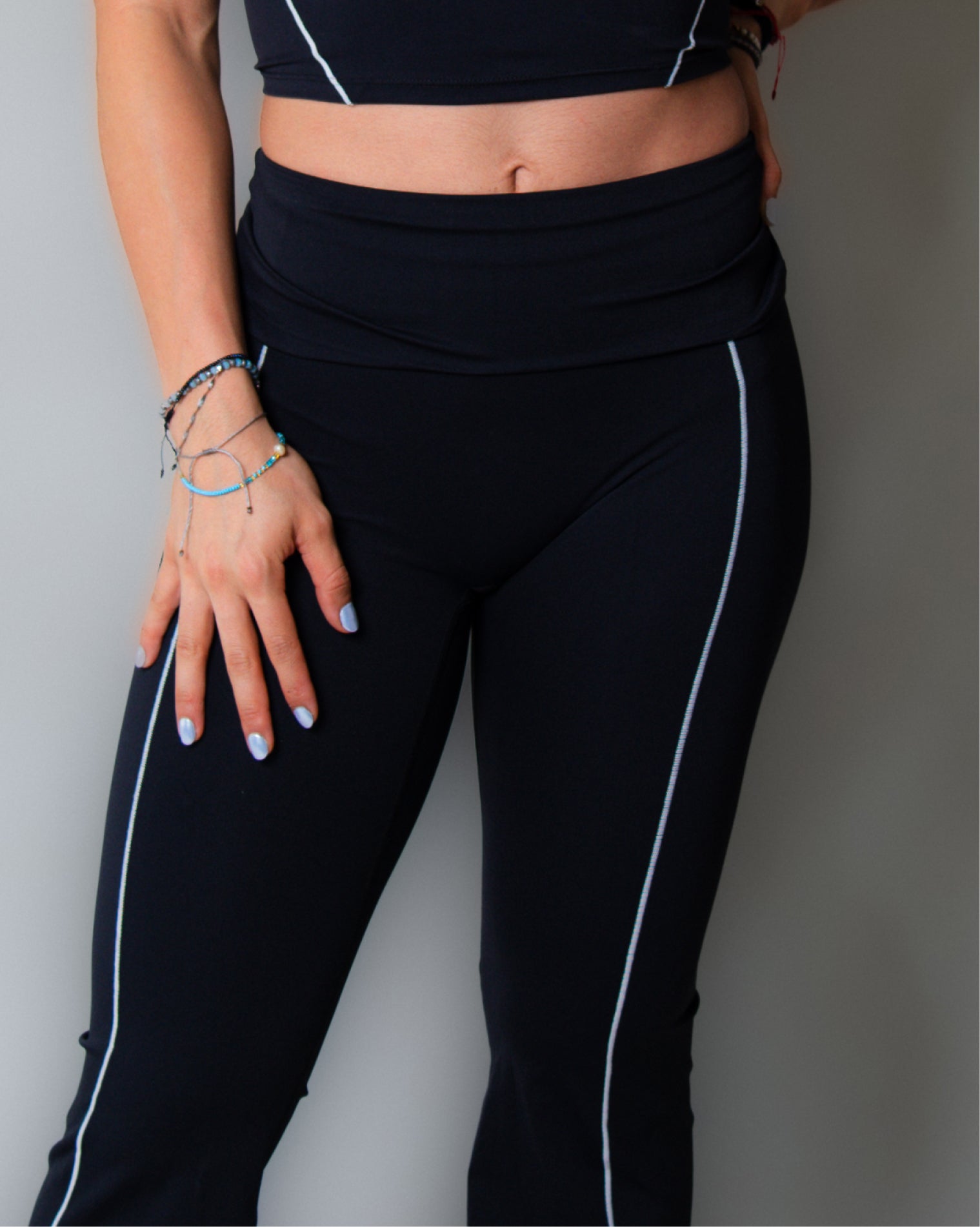 Leggings deportivos color negro de tiro alto con diseño liso y costuras visibles en contraste, ajuste ceñido al cuerpo y acabado uniforme, mostrados en vista posterior como parte de un conjunto deportivo.
