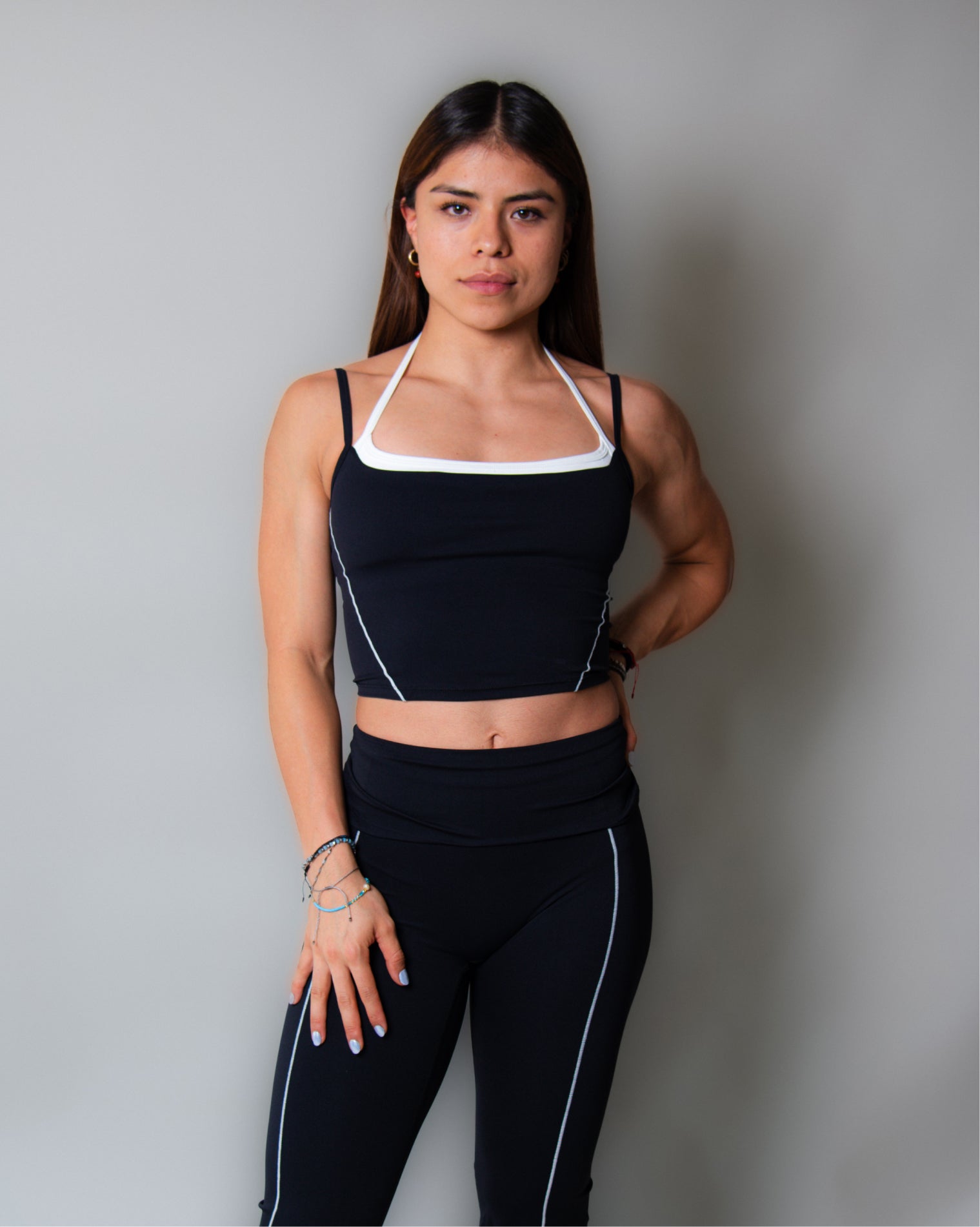 Leggings deportivos color negro de tiro alto con diseño liso y costuras visibles en contraste, ajuste ceñido al cuerpo y acabado uniforme, mostrados en vista posterior como parte de un conjunto deportivo.