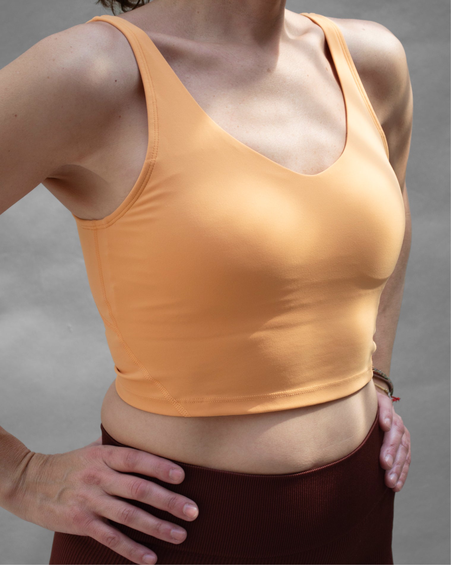 Top deportivo naranja tipo tank para mujer, con tirantes anchos y escote redondeado, mayor cobertura en el pecho y ajuste ceñido al cuerpo. Diseño liso de estilo deportivo, ideal para entrenar o usar en actividades diarias.