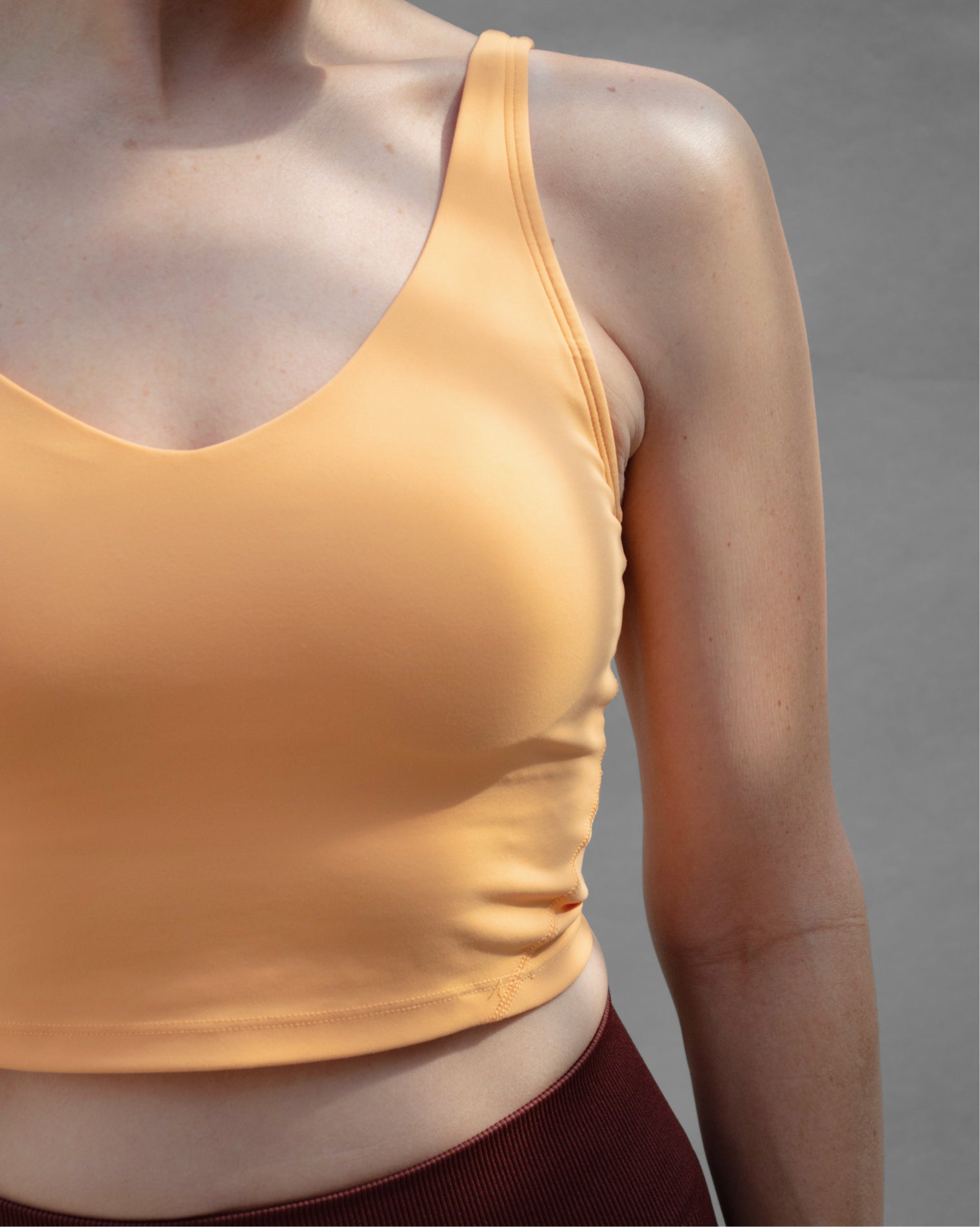 Top deportivo naranja tipo tank para mujer, con tirantes anchos y escote redondeado, mayor cobertura en el pecho y ajuste ceñido al cuerpo. Diseño liso de estilo deportivo, ideal para entrenar o usar en actividades diarias.