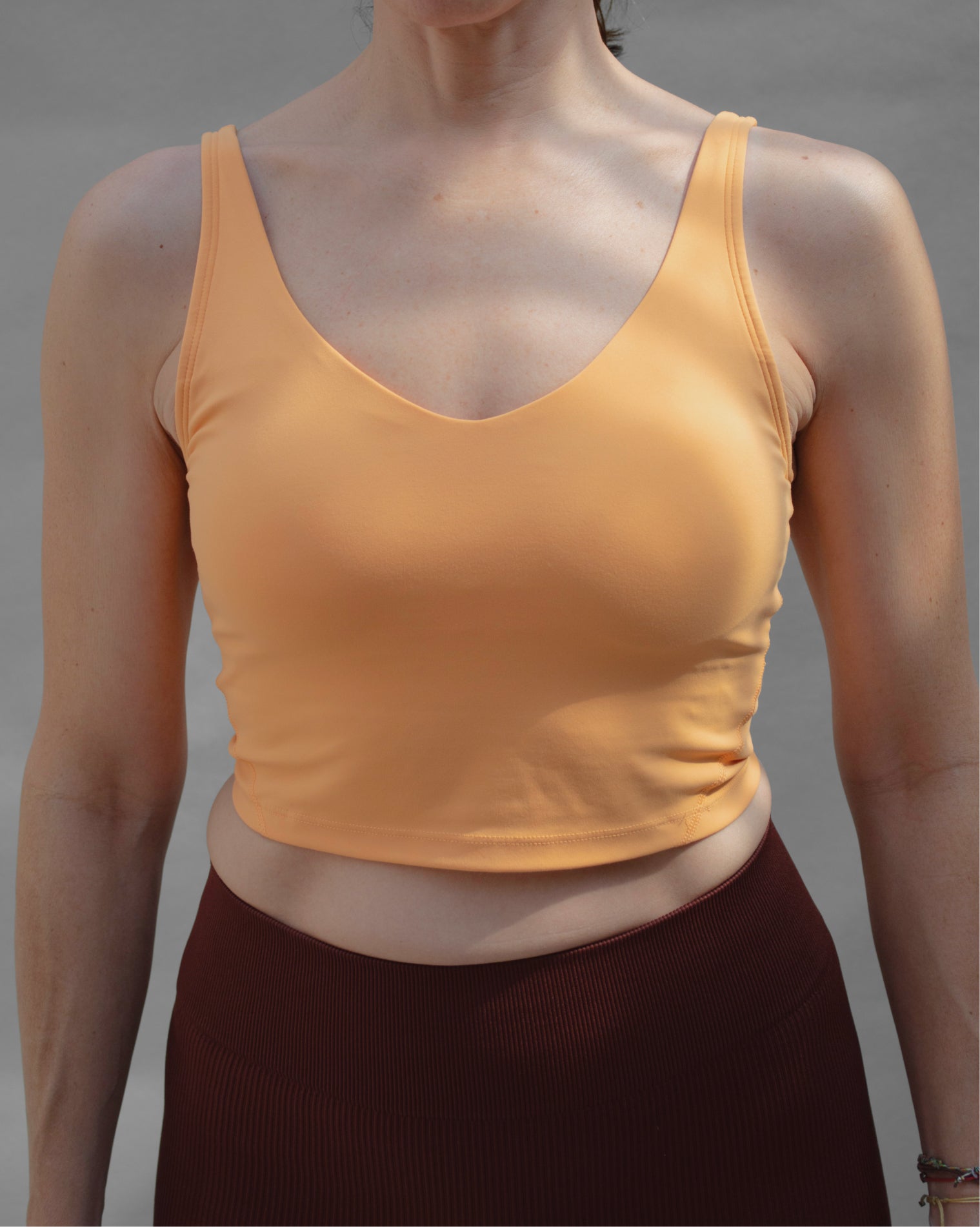 Top deportivo naranja tipo tank para mujer, con tirantes anchos y escote redondeado, mayor cobertura en el pecho y ajuste ceñido al cuerpo. Diseño liso de estilo deportivo, ideal para entrenar o usar en actividades diarias.