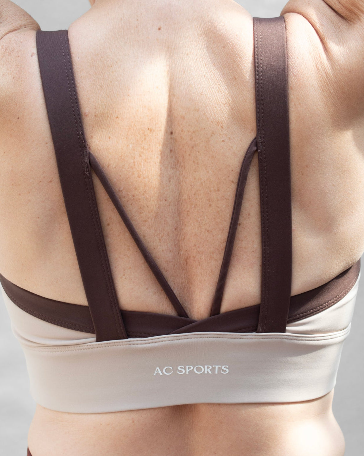 Top deportivo café para mujer con tirantes anchos en contraste color beige, escote redondeado y ajuste ceñido al cuerpo, diseño liso de estilo deportivo ideal para entrenamientos y uso diario.