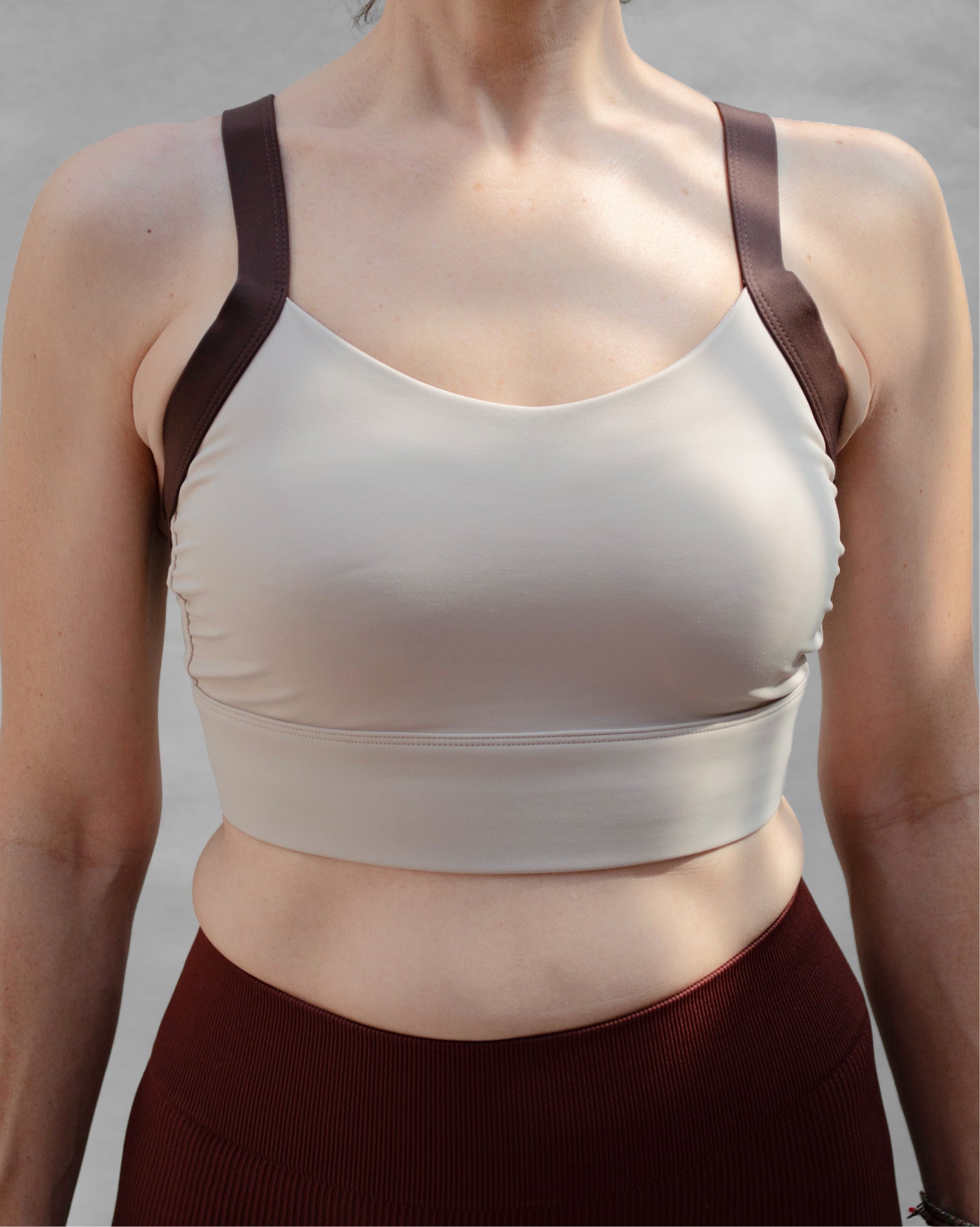Top deportivo café para mujer con tirantes anchos en contraste color beige, escote redondeado y ajuste ceñido al cuerpo, diseño liso de estilo deportivo ideal para entrenamientos y uso diario.
