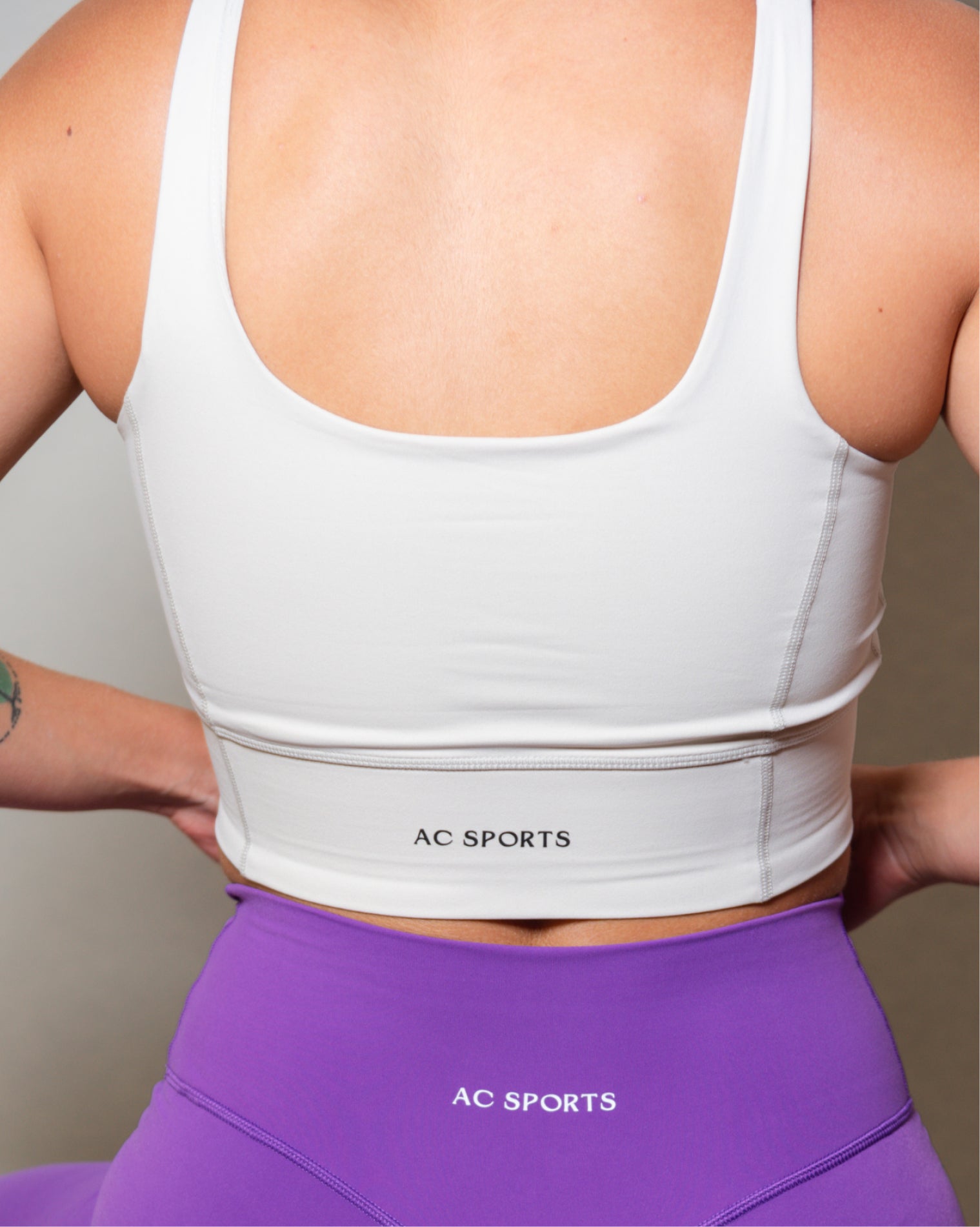 Top deportivo blanco para mujer con tirantes anchos, escote en forma de V y ajuste ceñido al cuerpo, diseño liso con banda inferior visible que aporta un ajuste firme, ideal para entrenamiento y uso diario.